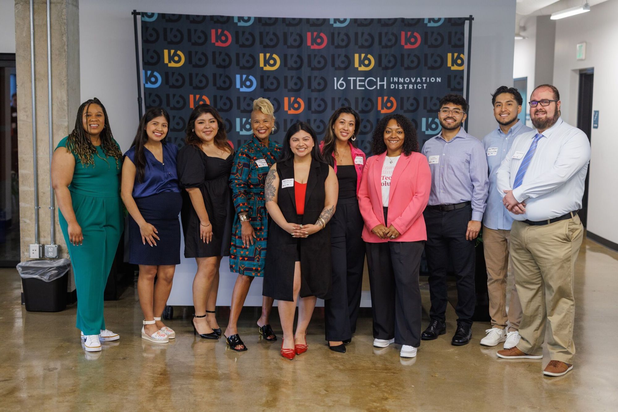 A group of eleven people smiling together in front of a 16 Tech Innovation District backdrop