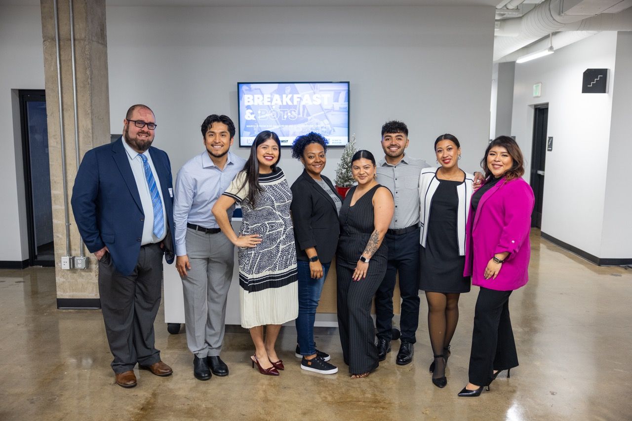 A group of nine people smiling together in front of a screen announcing Breakfast & Bots